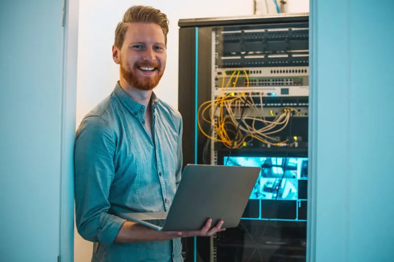 Male Caucasian IT technician using laptop in server room Jobs in der IT Branche